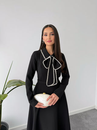 BLACK DRESS WITH PEARL EMBELLISHED COLLAR AND ASYMMETRICAL SKIRT.